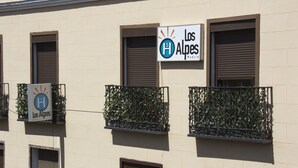 A building with multiple balconies, some with plants. There are signs indicating the name 'Los Alpes'. - Hostal Los Alpes (Madrid)