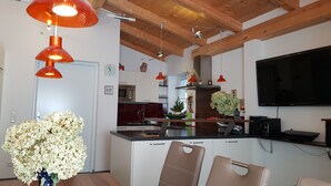 A modern kitchen with wooden beams, a dining area with a vase of flowers, and a TV mounted on the wall.