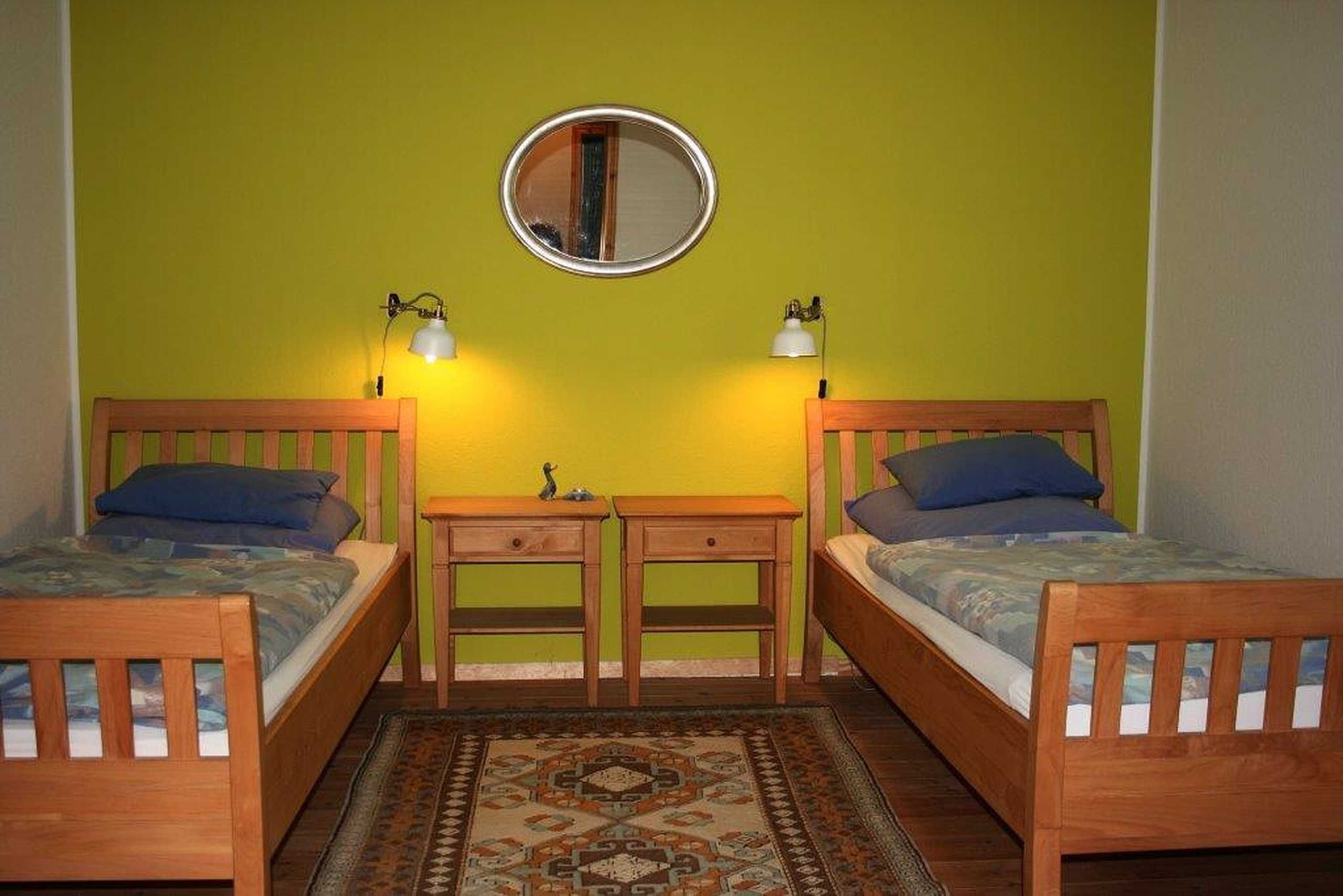 Une chambre avec deux lits en bois, une petite table, deux lampes de chevet, un miroir et un tapis à motifs.