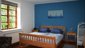 A bedroom with a wooden bed, a window with blinds, a painting on the wall, and a metal bunk bed.