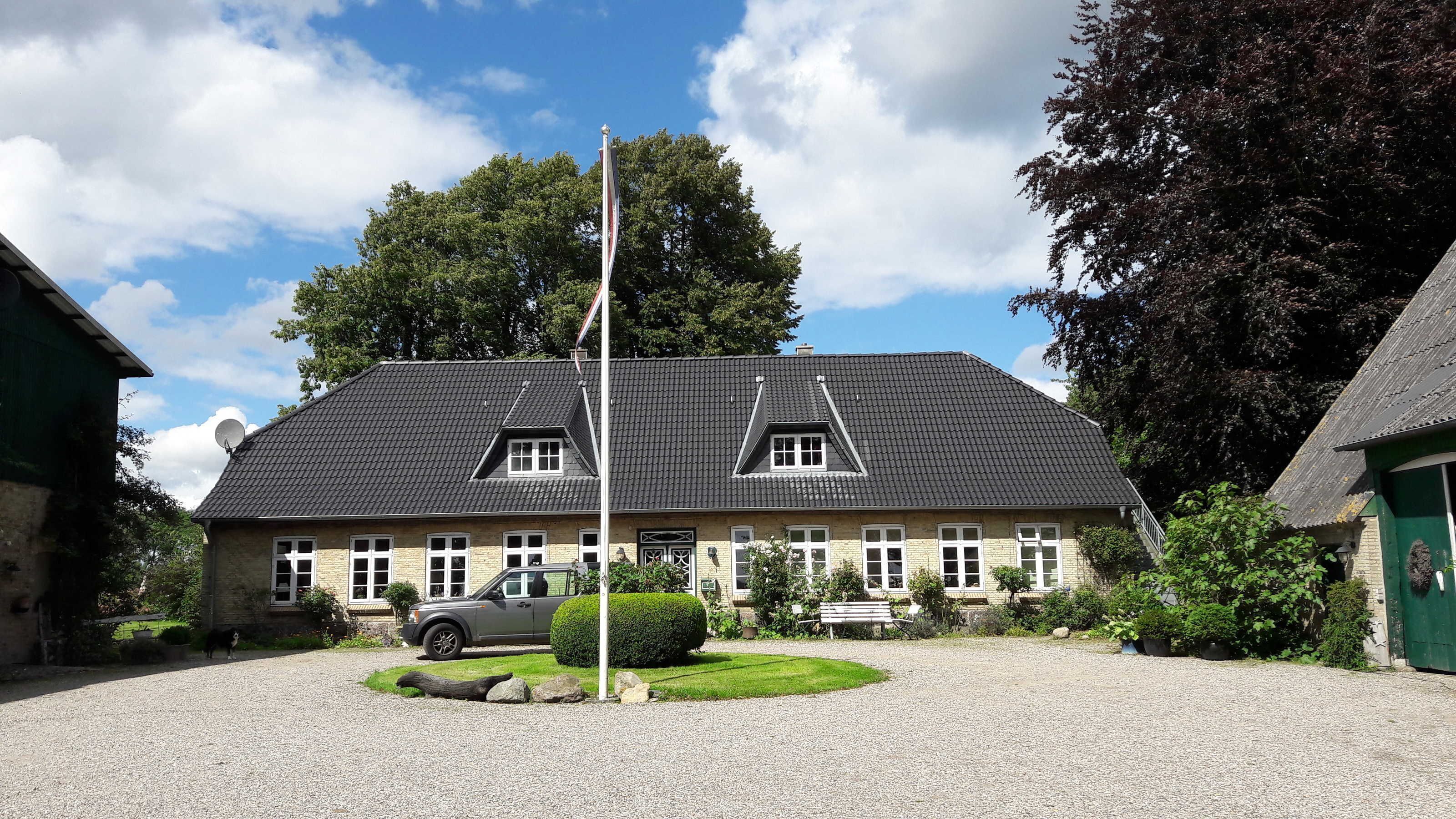 Une maison à deux étages, avec un toit recouvert de tuiles sombres, une allée et une pelouse.