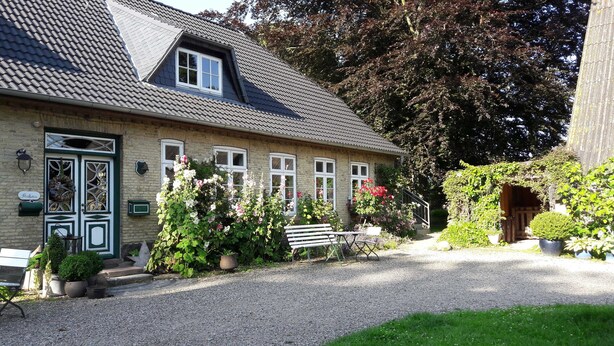 A traditional house with a gravel driveway, a bench, and potted plants.