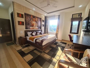 A hotel room with a large bed, a desk, a chair, a TV, and a window with a view.