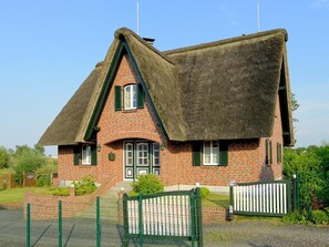 Ein traditionelles Backsteinhaus mit einem steilen Strohdach und einer kleinen Veranda.