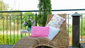 Uma cadeira de vime com almofada branca e rosa sobre um deck de madeira.
