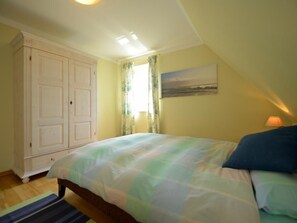 A bedroom with a bed, a wardrobe, a window with curtains, and a painting on the wall.
