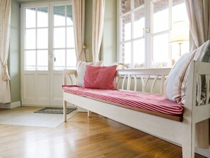 Una habitación con piso de madera, un banco blanco con ropa de cama a rayas y una ventana con cortinas.