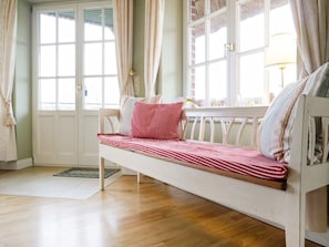 A room with a wooden floor, a white bench with striped bedding, and a window with curtains.