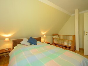 Ein Schlafzimmer mit einem großen Bett, einem Babybett, zwei Nachttischlampen und einer Tür.