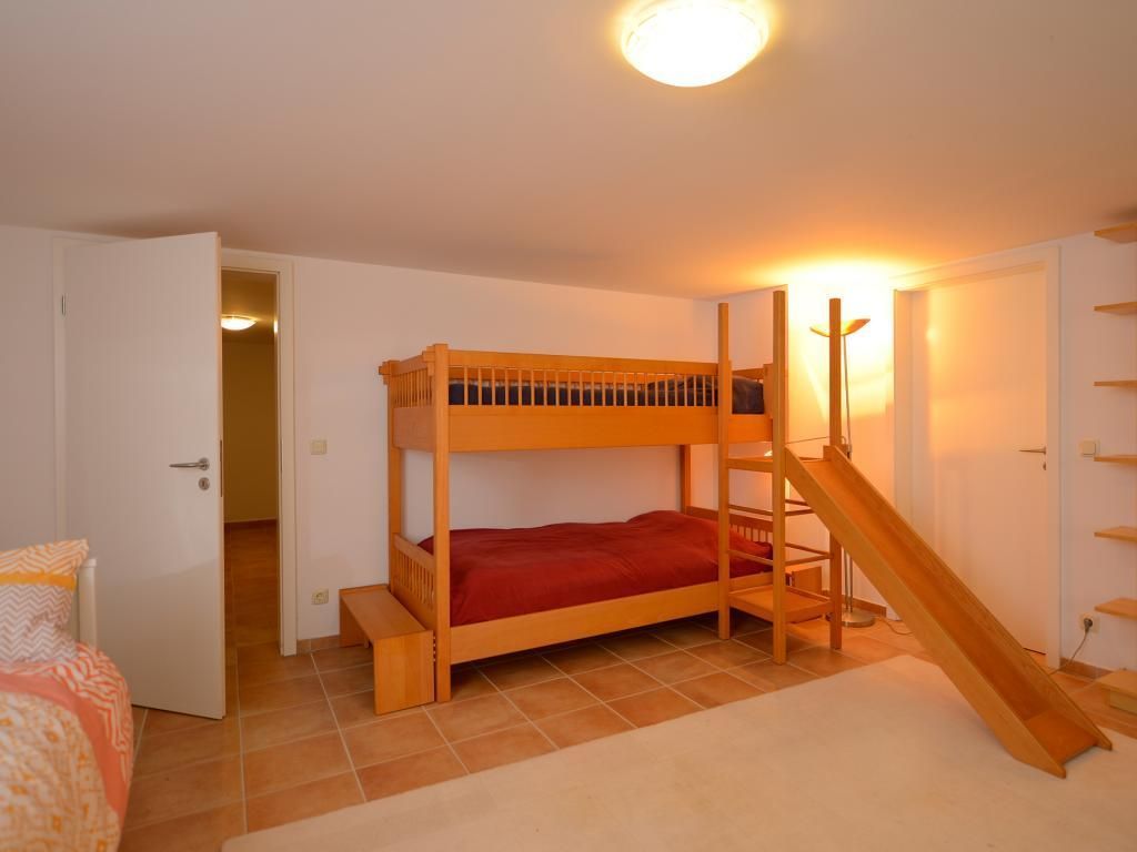 Un lit superposé avec une échelle en bois et un petit toboggan, une porte blanche et un sol carrelé.