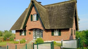 A traditional brick house with a steeply pitched thatched roof and a small front porch.