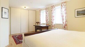 Quarto com cama, escrivaninha, cadeira, janela com cortinas florais e um quadro na parede.
