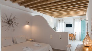 Un dormitorio con una cama grande, mesitas de noche, un televisor montado en la pared y una zona de comedor con mesa y sillas.
