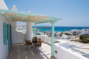 A terrace with a table and chairs, overlooking a coastal town with white buildings and the sea.