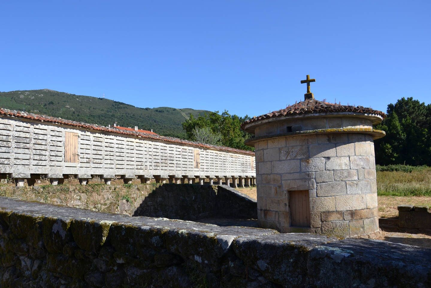 A stone bridge with a small tower featuring a cross on top, leading to a building with a tiled roof.