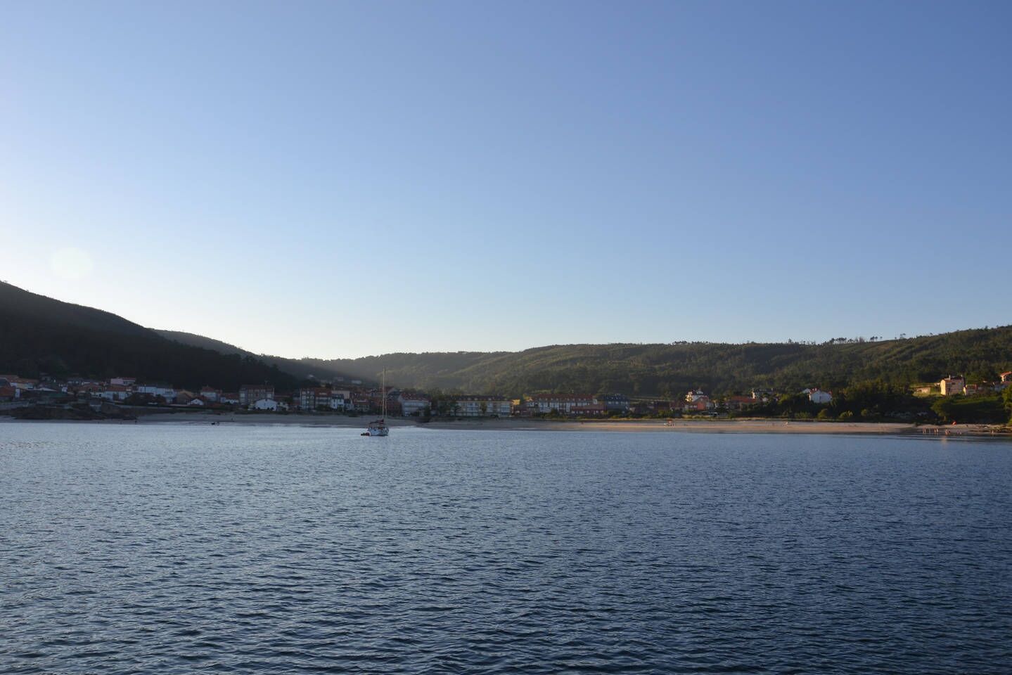 Ein ruhiger See mit einem Boot in der Mitte, umgeben von Hügeln und Gebäuden.