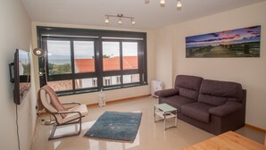 A living room with a large window, a brown sofa, a small table, and a chair.