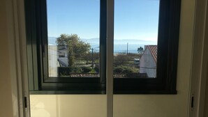 A room with a sliding glass door leading to a balcony with a view of the sea and buildings.