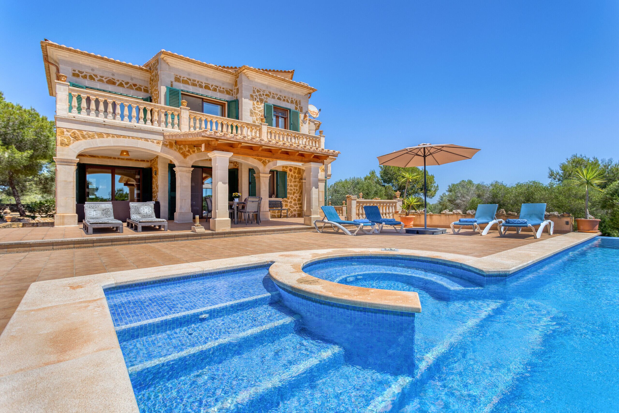 Une grande maison avec une piscine, un espace extérieur aménagé et un ciel d’un bleu éclatant.