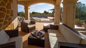 An outdoor seating area with wicker furniture, a pool, and a stone wall in the background.