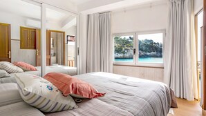 A bedroom with a large bed, a mirror, a window with a view of a beach, and wooden furniture.