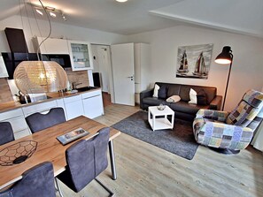 Un espace de vie compact comprenant un coin cuisine, un coin repas, un canapé et un fauteuil.