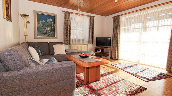 Ein Wohnzimmer mit Sofa, Couchtisch, Fernseher und Teppichen mit Muster.