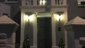A hotel entrance with a dark door, two lit windows, and a sign above the door.