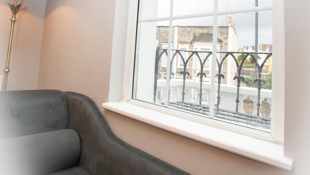 A room with a curved grey sofa, a floor lamp, and a large arched window with a view of a bridge and buildings.
