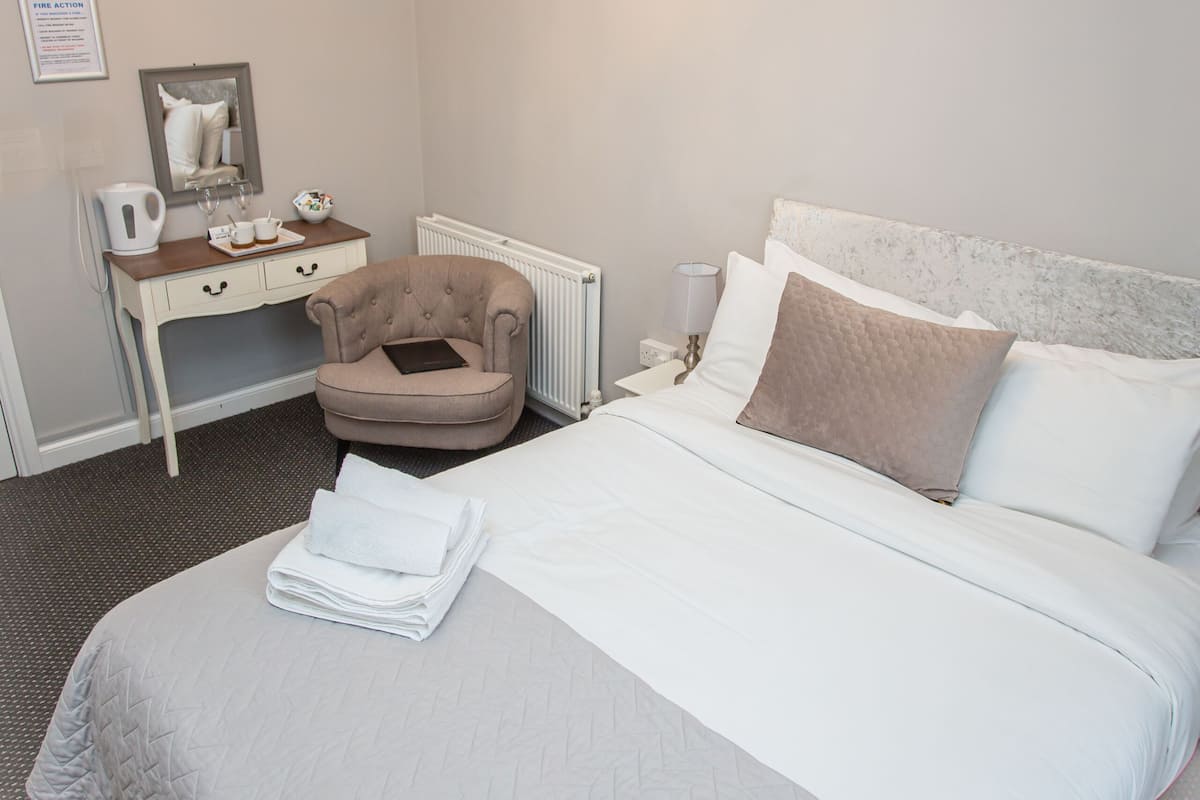 A neatly arranged hotel room with a bed, a chair, a desk, and a chandelier.