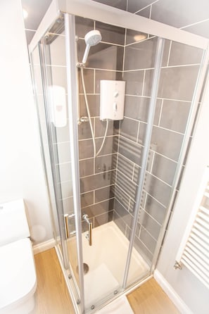 A glass-enclosed shower with a handheld showerhead and a wall-mounted control panel. - The Ibrox Lodge (Bristol)