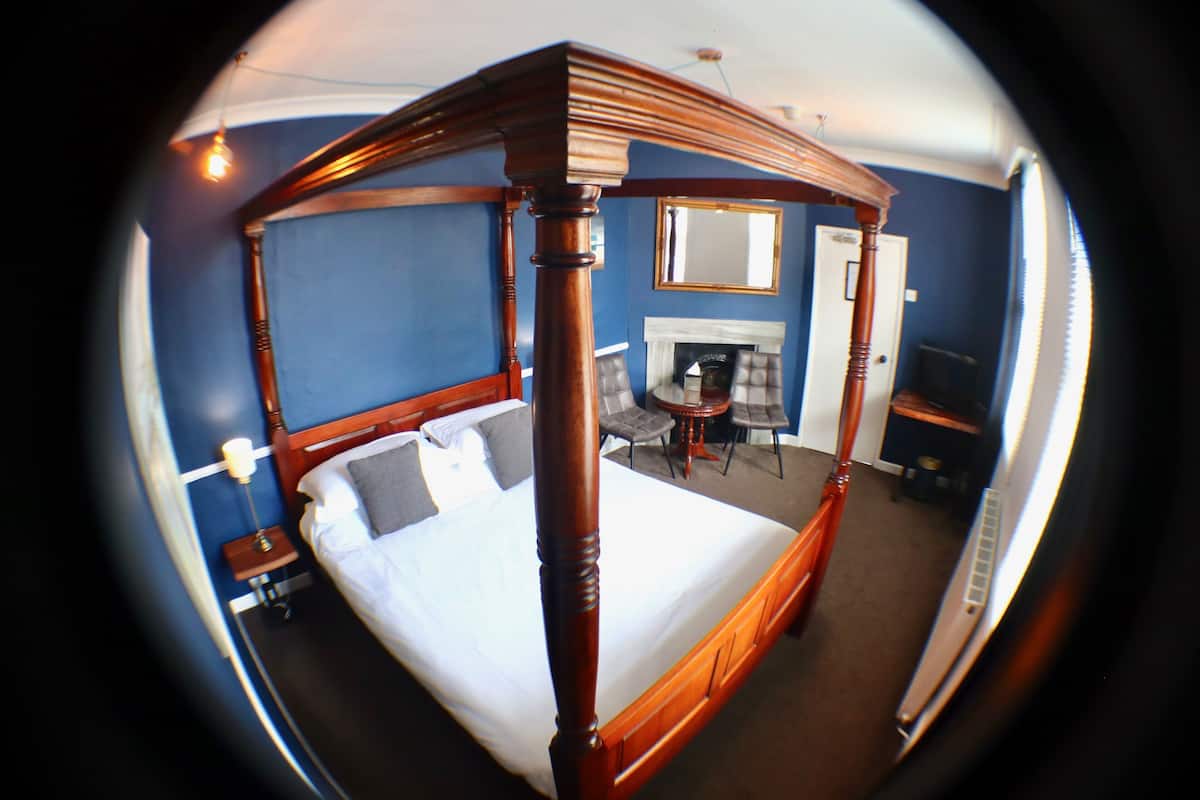 A room with a four-poster bed, a fireplace, a small round table with chairs, and a mirror on the wall.