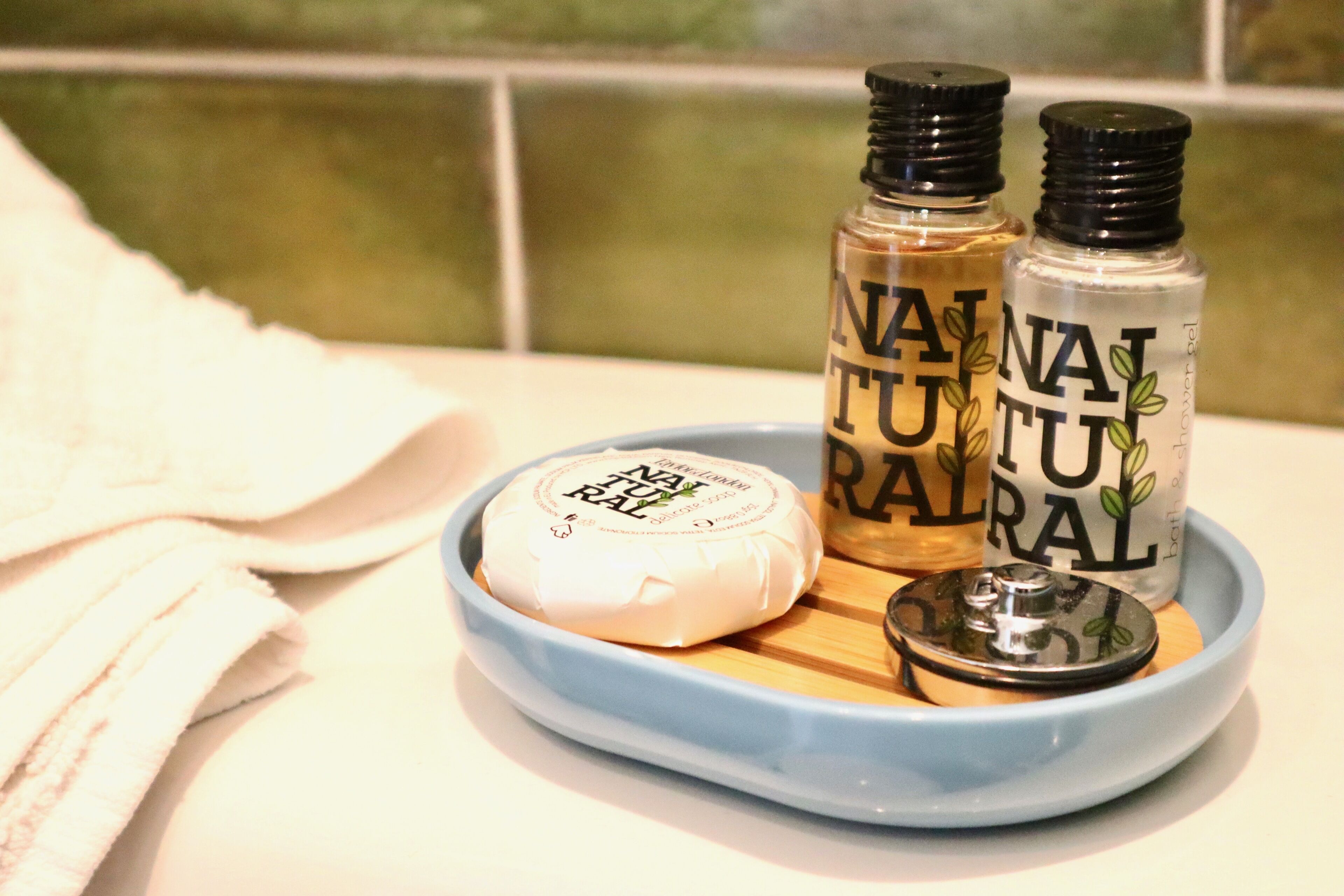 A bathroom counter with a blue tray holding a bar of soap, two bottles of lotion, and a container of shower gel.
