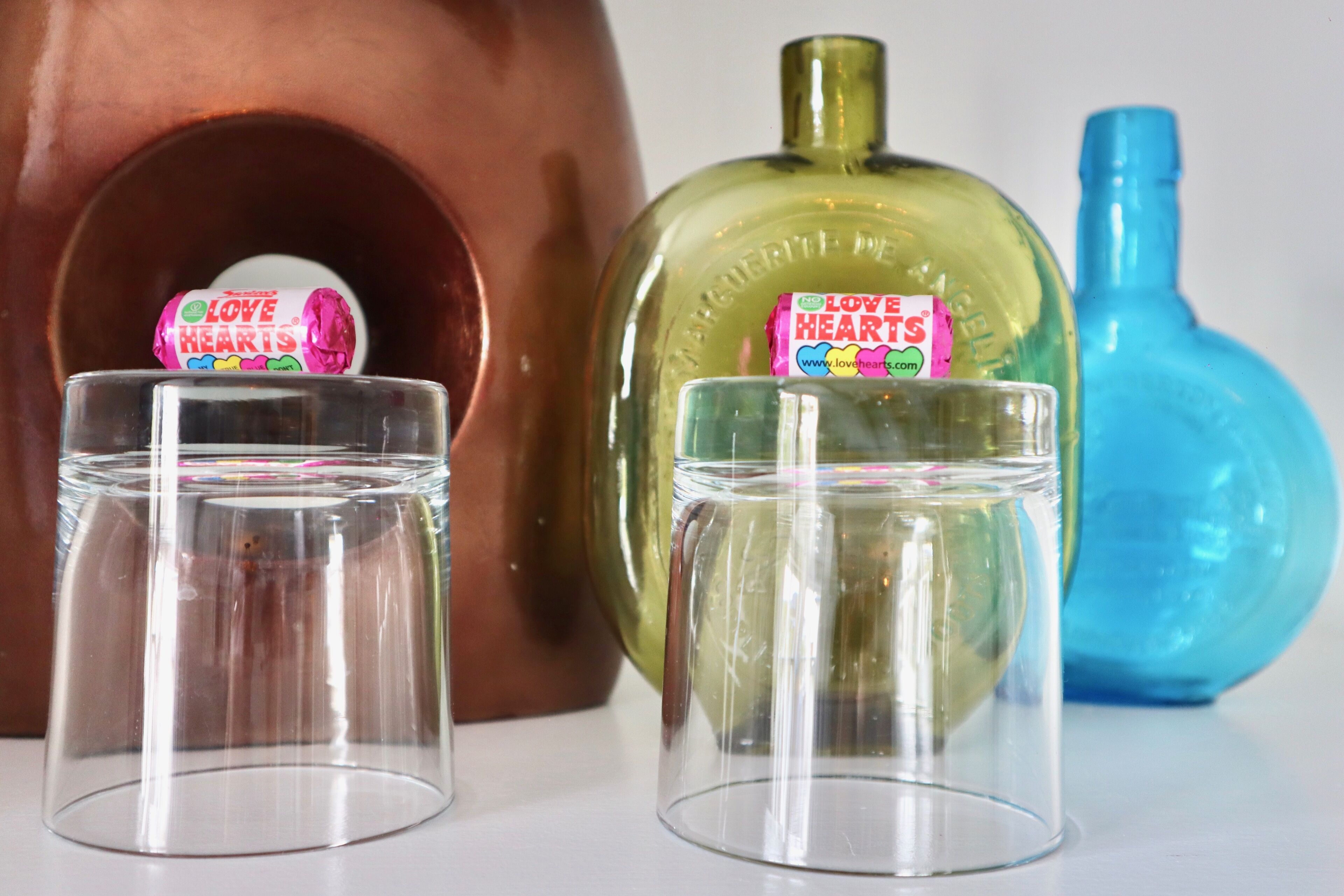 Tres recipientes de vidrio con etiqueta 'Love Hearts', colocados frente a una botella de cobre y otra verde.
