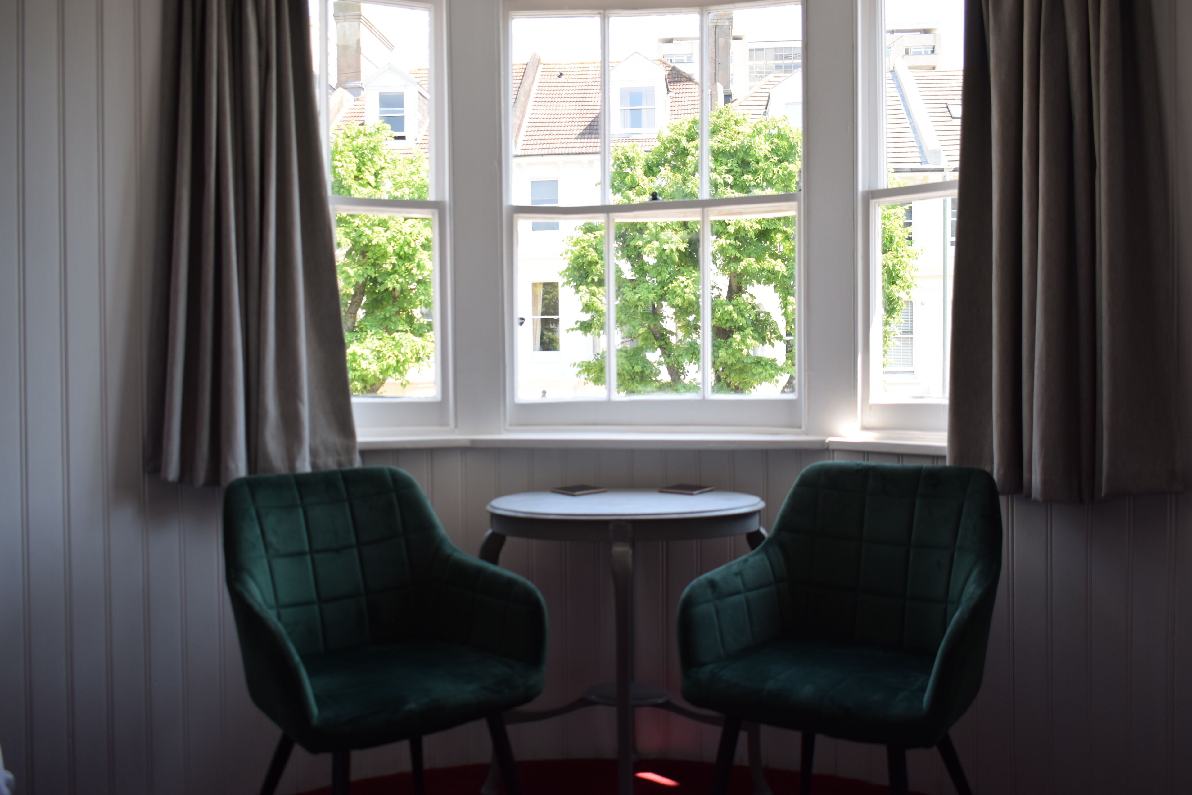 A room with two green chairs and a small table by a window with curtains.
