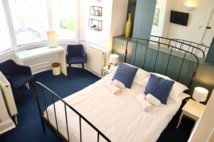 A hotel room with a bed, two chairs, a window, a radiator, a TV, and a staircase.