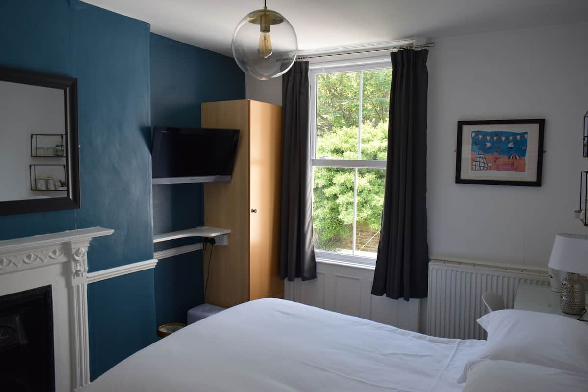 A hotel room with a bed, a TV, a fireplace, a window with curtains, and a framed picture on the wall.