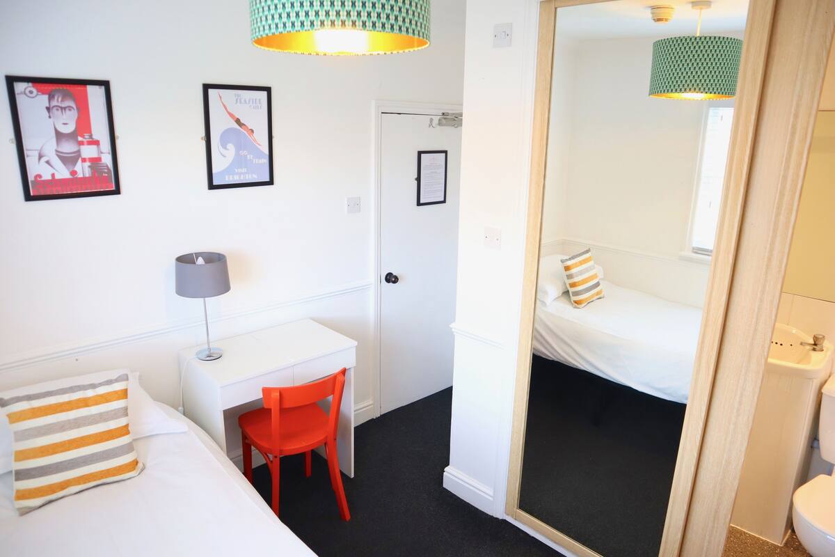 A compact hotel room with a bed, a desk, a chair, and a bathroom visible through an open door.