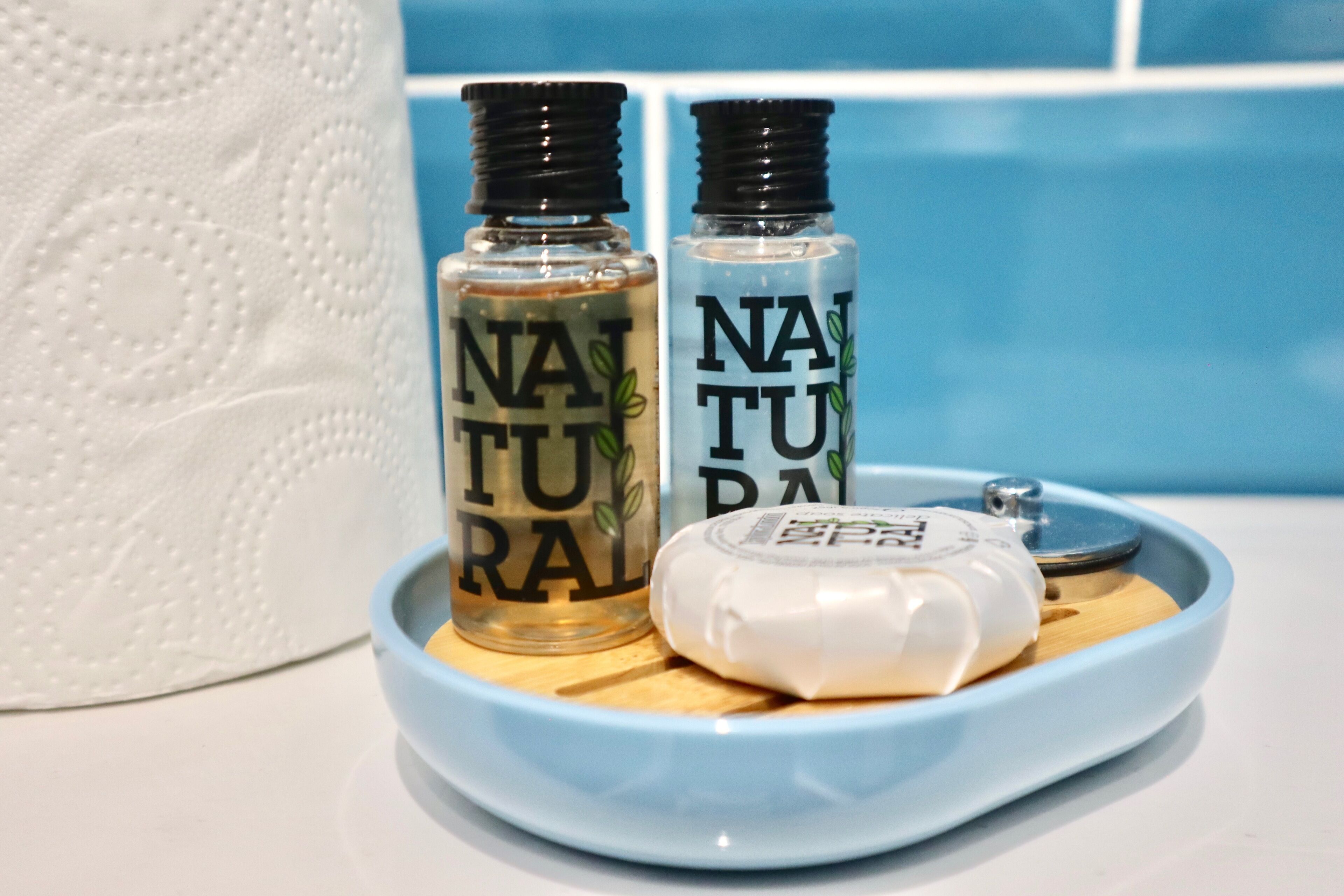 Two bottles of 'NATURAL' on a blue tray with a white container and a wooden object.