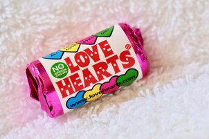 Paquete de caramelo enrollado con la etiqueta 'LOVE HEARTS' sobre una superficie blanca texturizada.