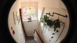 Una escalera con barandilla de madera, un candelabro y un ventanal con vista a un edificio.