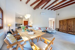Uma sala de estar ampla com uma mesa de jantar de madeira, sofás e uma cozinha ao fundo.