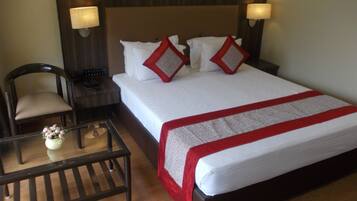 A hotel room with a bed, a chair, a nightstand, a lamp, and a small table with a vase.