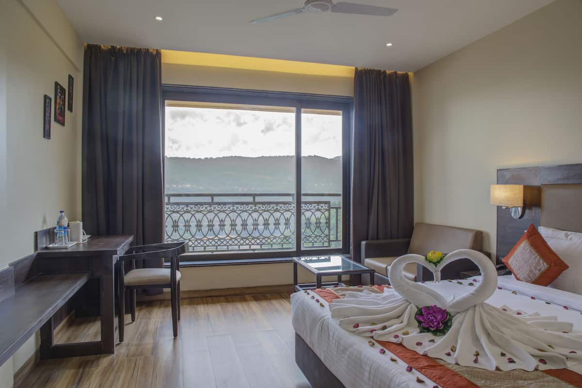 Habitación de hotel con cama, escritorio, silla, mesita y vista al mar a través de un ventanal grande.