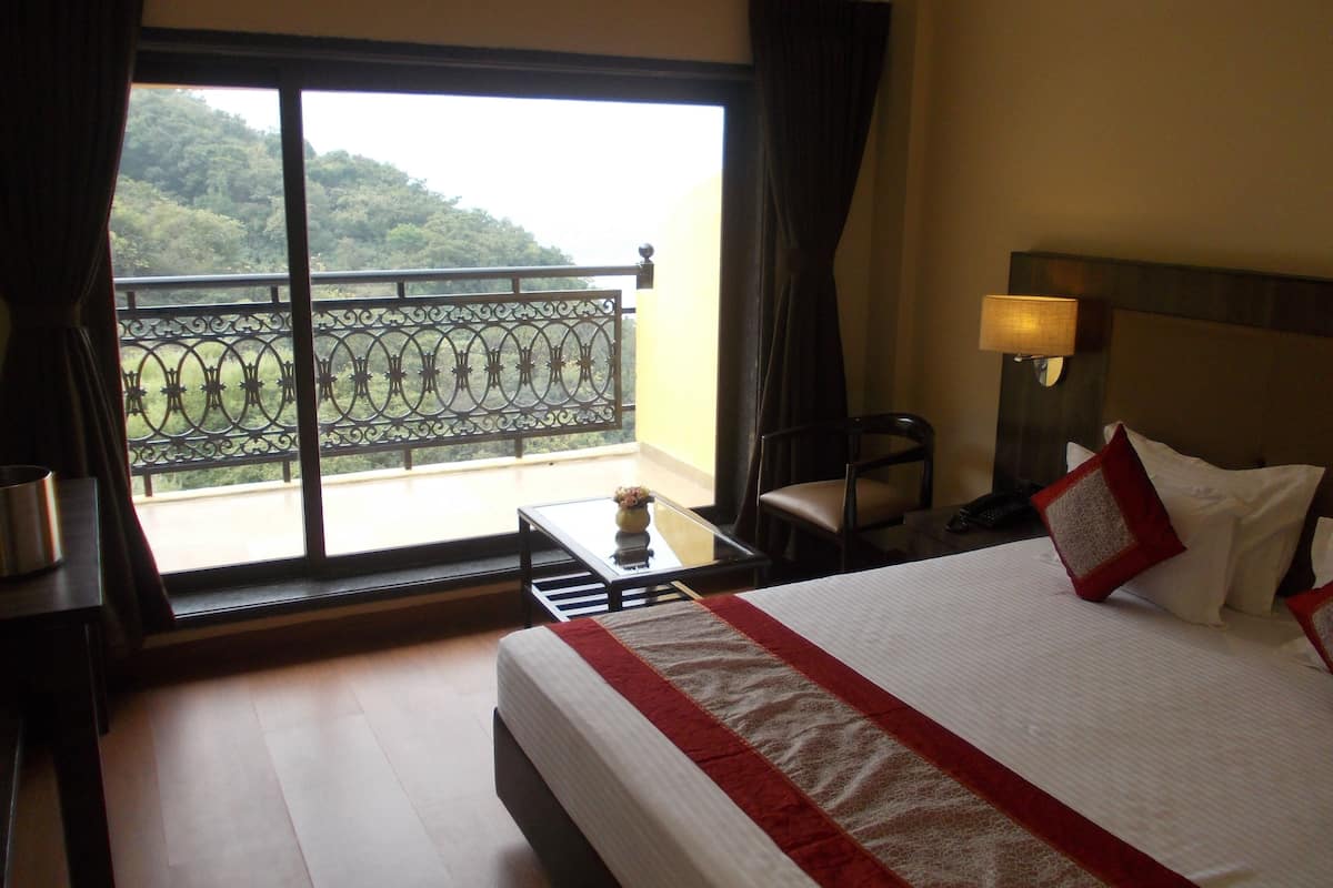 Habitación de hotel con una cama grande, un escritorio con lámpara, una silla y vistas a un balcón con barandilla.