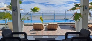 A poolside area with lounge chairs, a pool, and a view of the ocean.