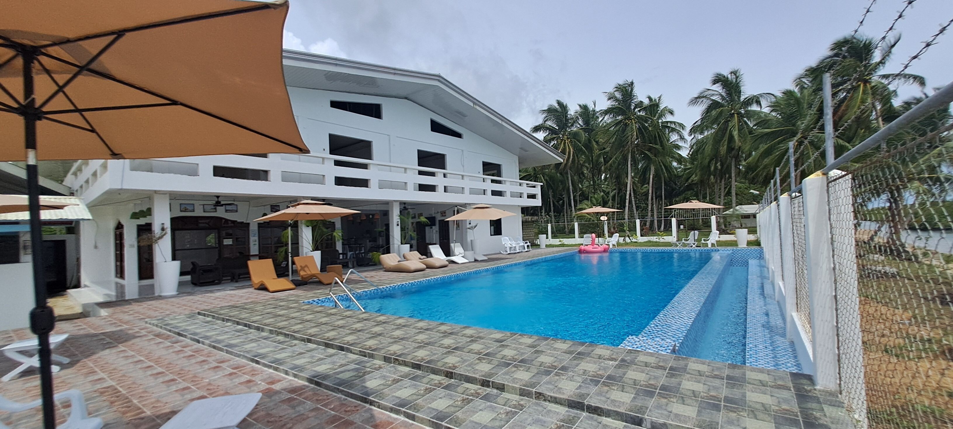 A hotel with a swimming pool, lounge chairs, and umbrellas.