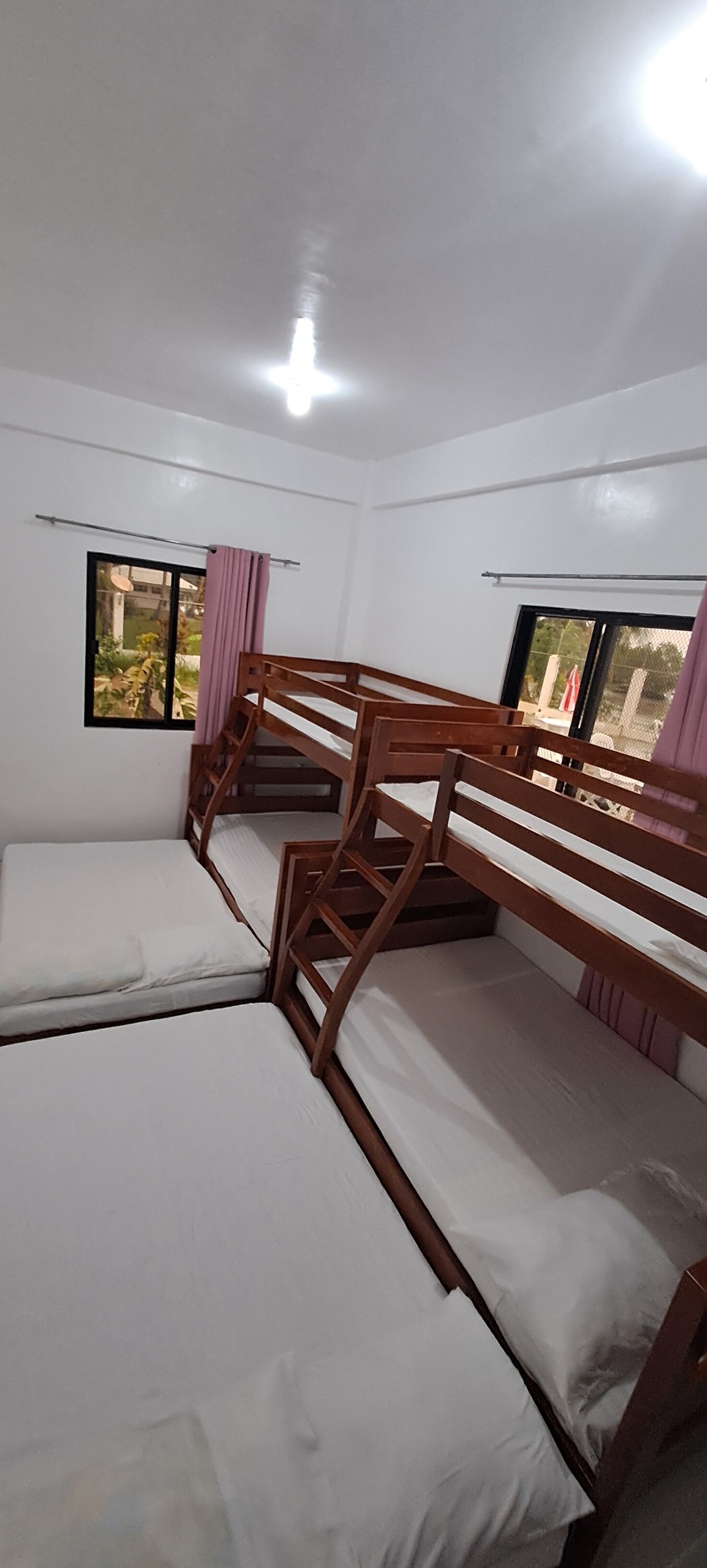 A room with bunk beds, a window with a curtain, and a view of the outside.