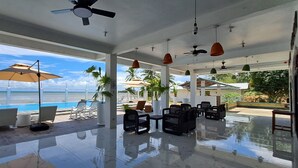 A spacious indoor area with a pool, chairs, and umbrellas, overlooking a clear blue ocean. -  Chilly Beach Resort Palawan (Aborlan)