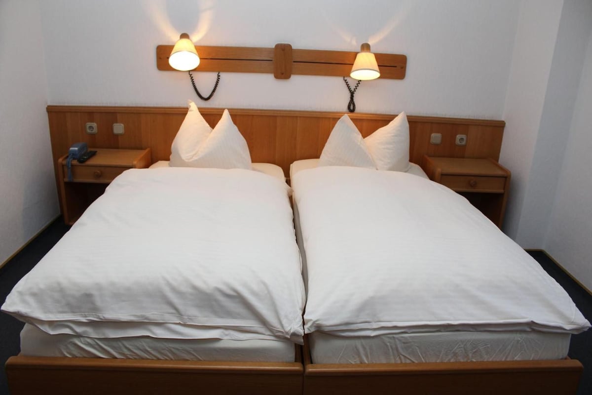 Un lit double avec deux tables de chevet, chacune équipée d’une lampe, dans une chambre dont la tête de lit et les lampes murales sont en bois.